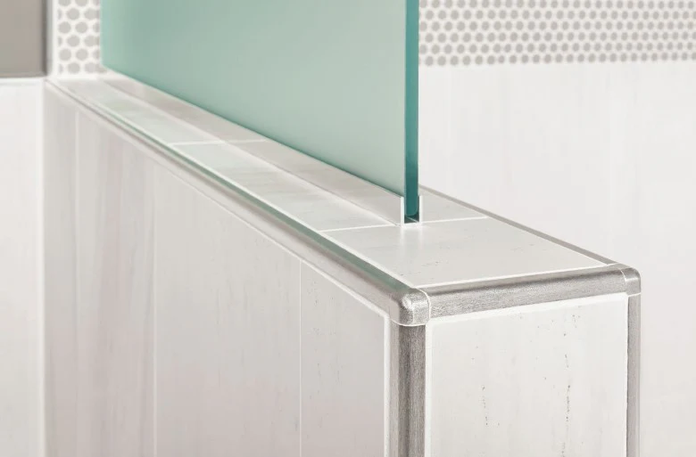 Close-up of a Schluter Rondec tile edge trim installed on a tiled surface, showcasing its curved metal profile and clean finish.